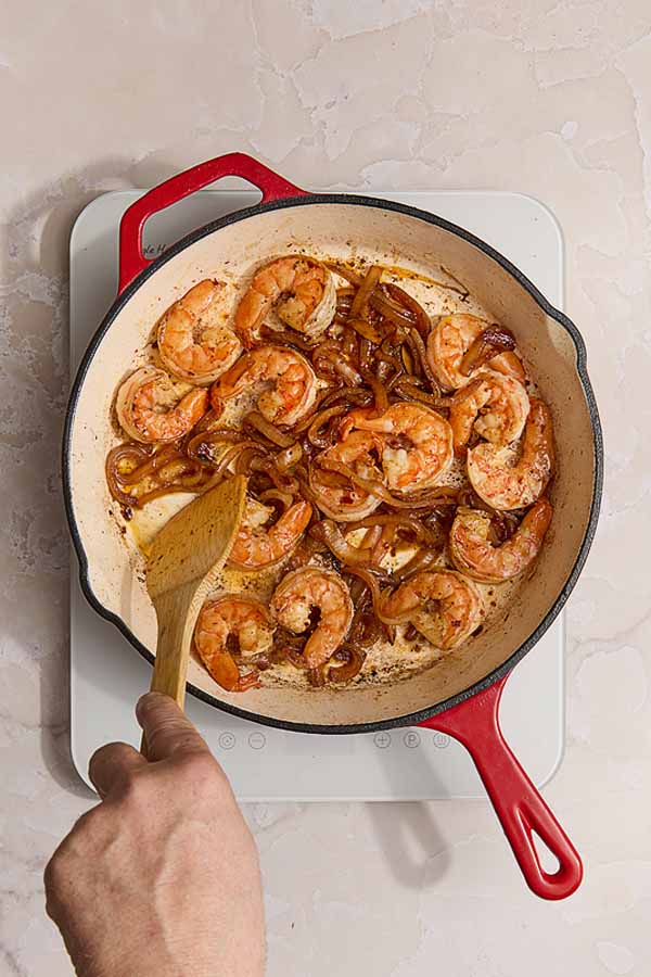 Shrimp and caramelized onions cooking together in a skillet, turning pink and golden for shrimp and chorizo.