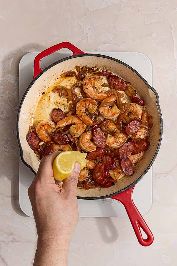 Cooked shrimp, onions, and chorizo in a skillet being finished with a squeeze of lemon.
