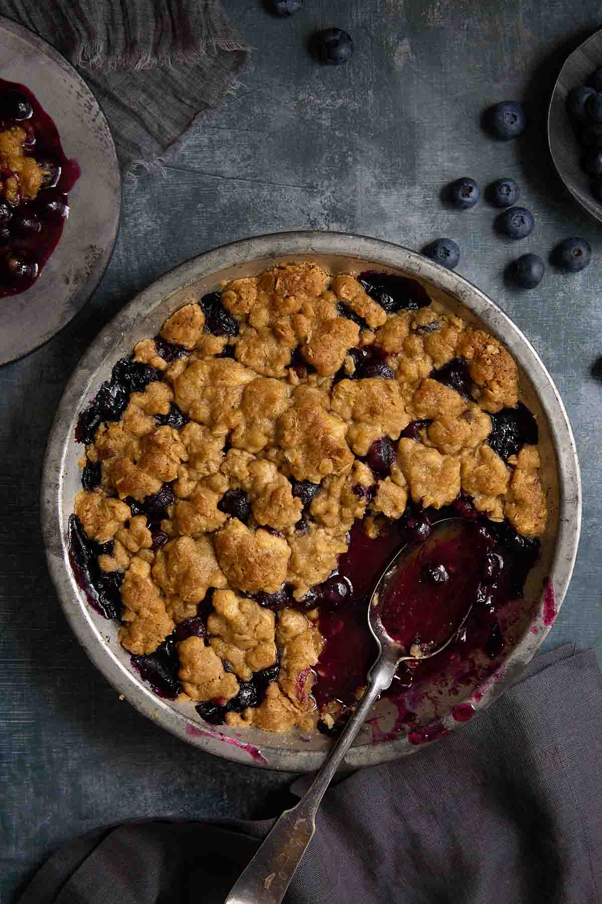 A full pan of baked blueberry crumble with a serving spoon inside.