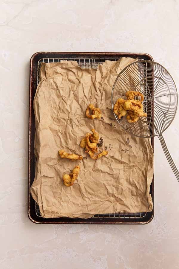 Freshly fried clams being placed onto a wire rack lined with brown paper to drain excess oil.