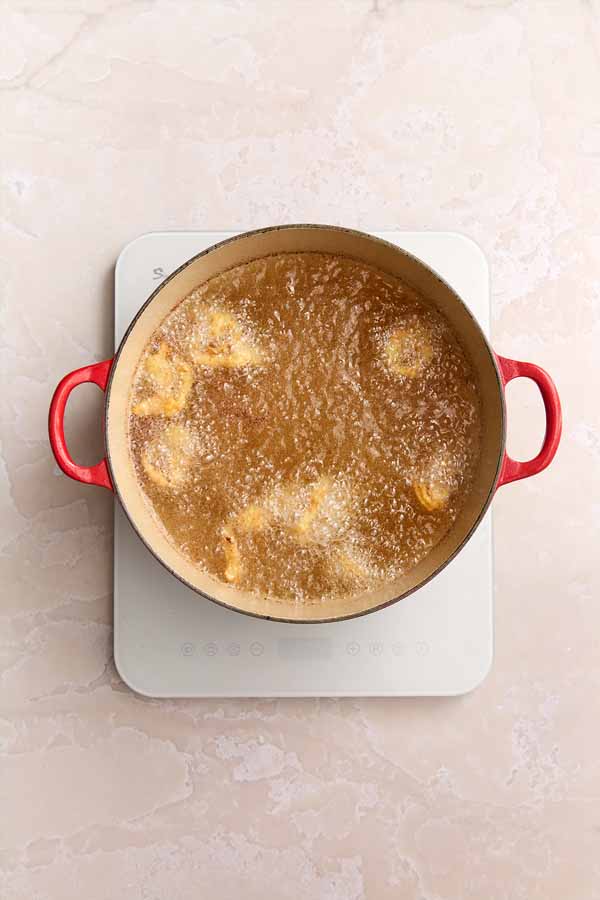 Fried clams bubbling in hot peanut oil in a red Dutch oven, cooking evenly.