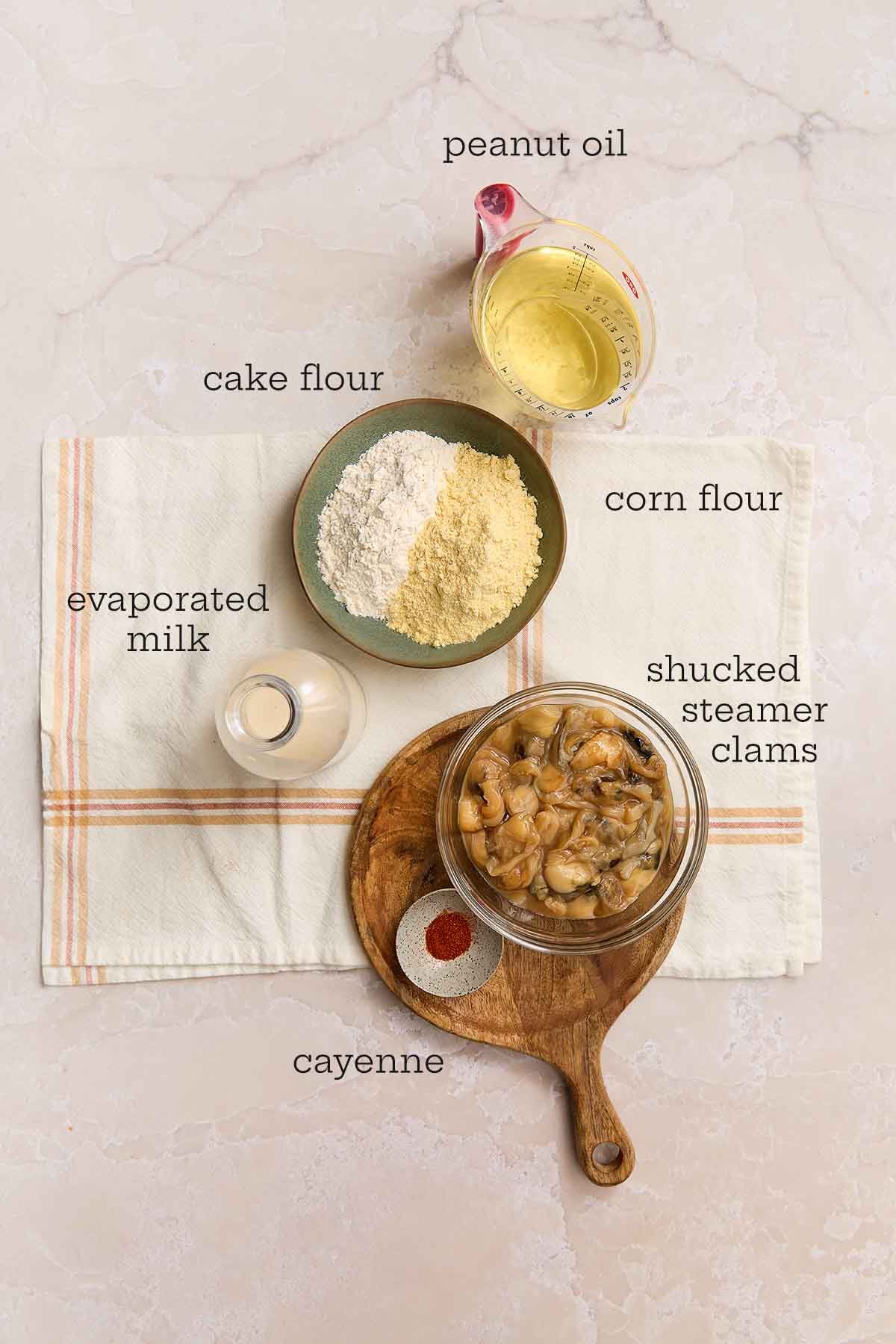 Ingredients for fried clams including peanut oil, cake flour, corn flour, evaporated milk, shucked steamer clams, and cayenne arranged on a counter.