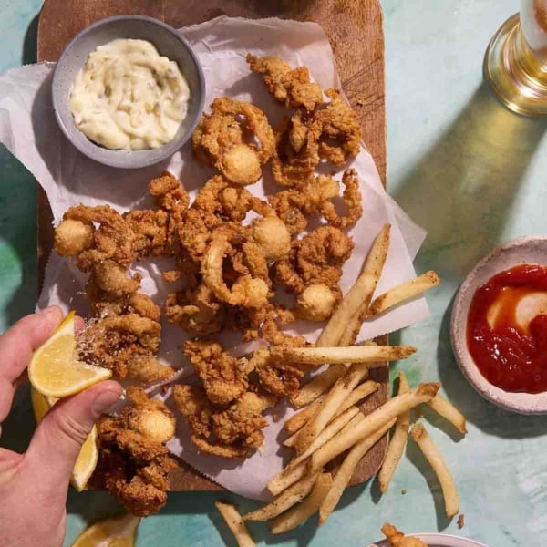 A square overhead shot of crispy fried whole belly clams, French fries, lemon, and dipping sauces.