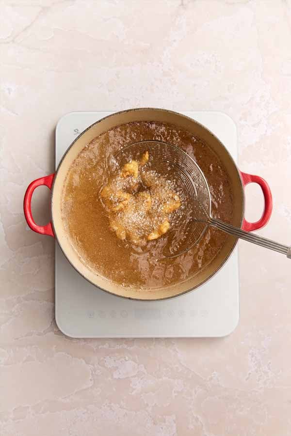 A wire-mesh skimmer lifting crispy fried clams from bubbling hot oil in a red Dutch oven.