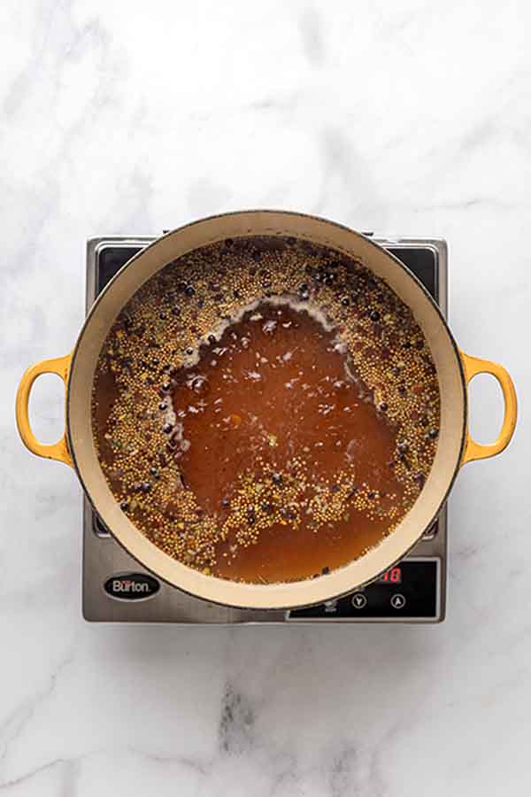 A yellow pot of brown brining liquid with whole spices boiling on an induction burner.
