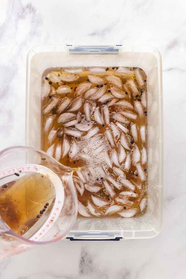 Brine being poured from a measuring cup into a plastic container with ice and cold water.
