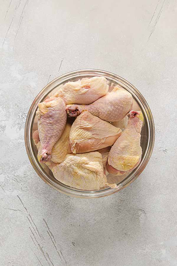 Raw chicken pieces brining in a saltwater solution in a large glass bowl.