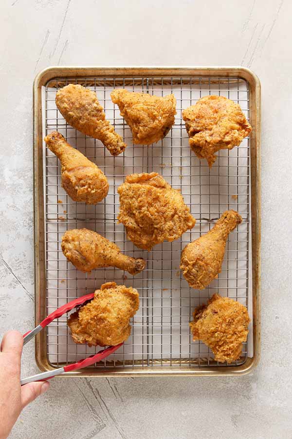 Golden, crispy fried chicken pieces draining on a wire rack set over a baking sheet.