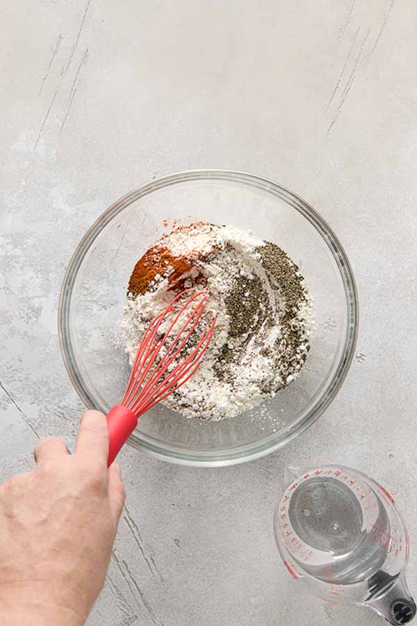 A hand whisking flour and spices together in a glass bowl for the batter.