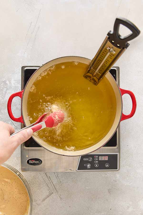 Using tongs to lower a piece of battered chicken into a pot of hot oil.