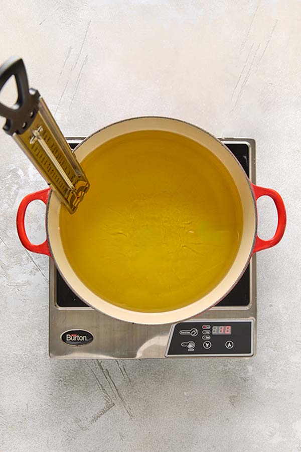 A Dutch oven filled with vegetable oil and a fry thermometer heating on a cooktop.