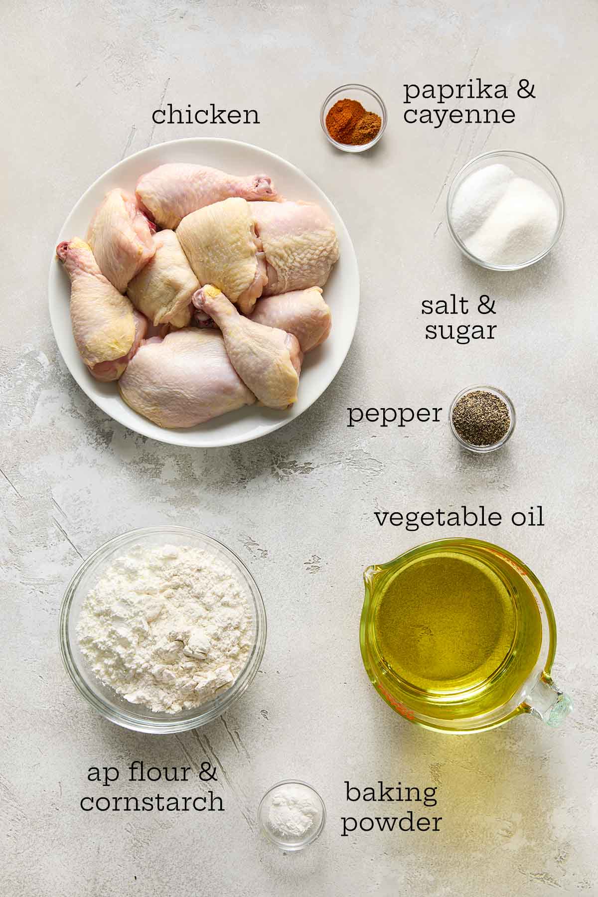 Ingredients for batter-fried chicken, including chicken, flour, spices, and oil, arranged on a counter.