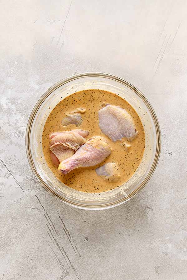 Raw chicken pieces marinating in a seasoned batter in a glass bowl.