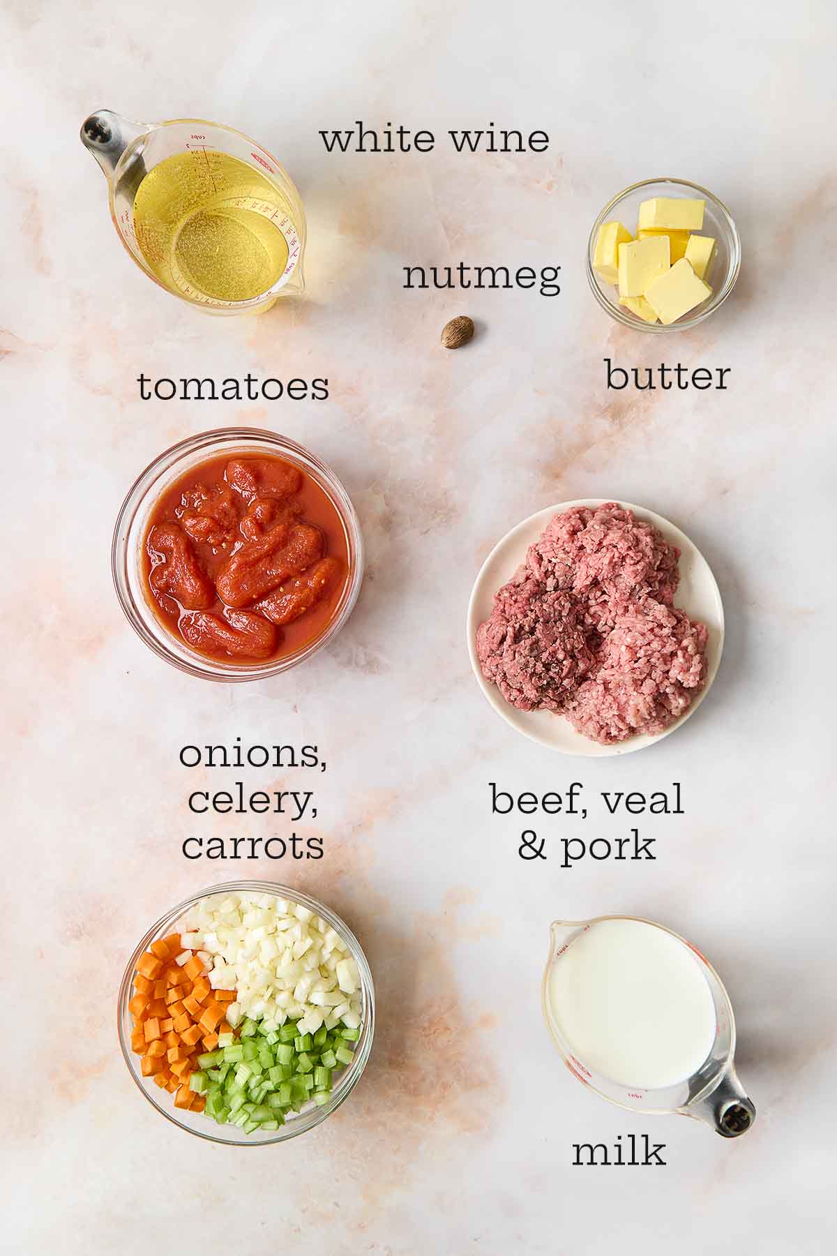 Fresh ingredients for Marcella Hazan Bolognese sauce, including chopped onions, carrots, celery, meat, wine, and tomatoes.