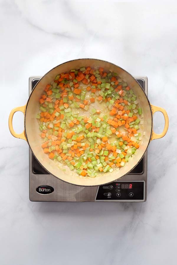 Chopped celery and carrots added to sautéed onions in a Dutch oven, forming the soffritto base.