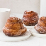 A square image of three fresh morning buns on individual plates, covered in sugar.