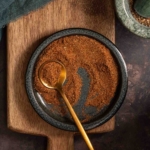 A small bowl of homemade Old Bay seasoning on a wooden cutting board.