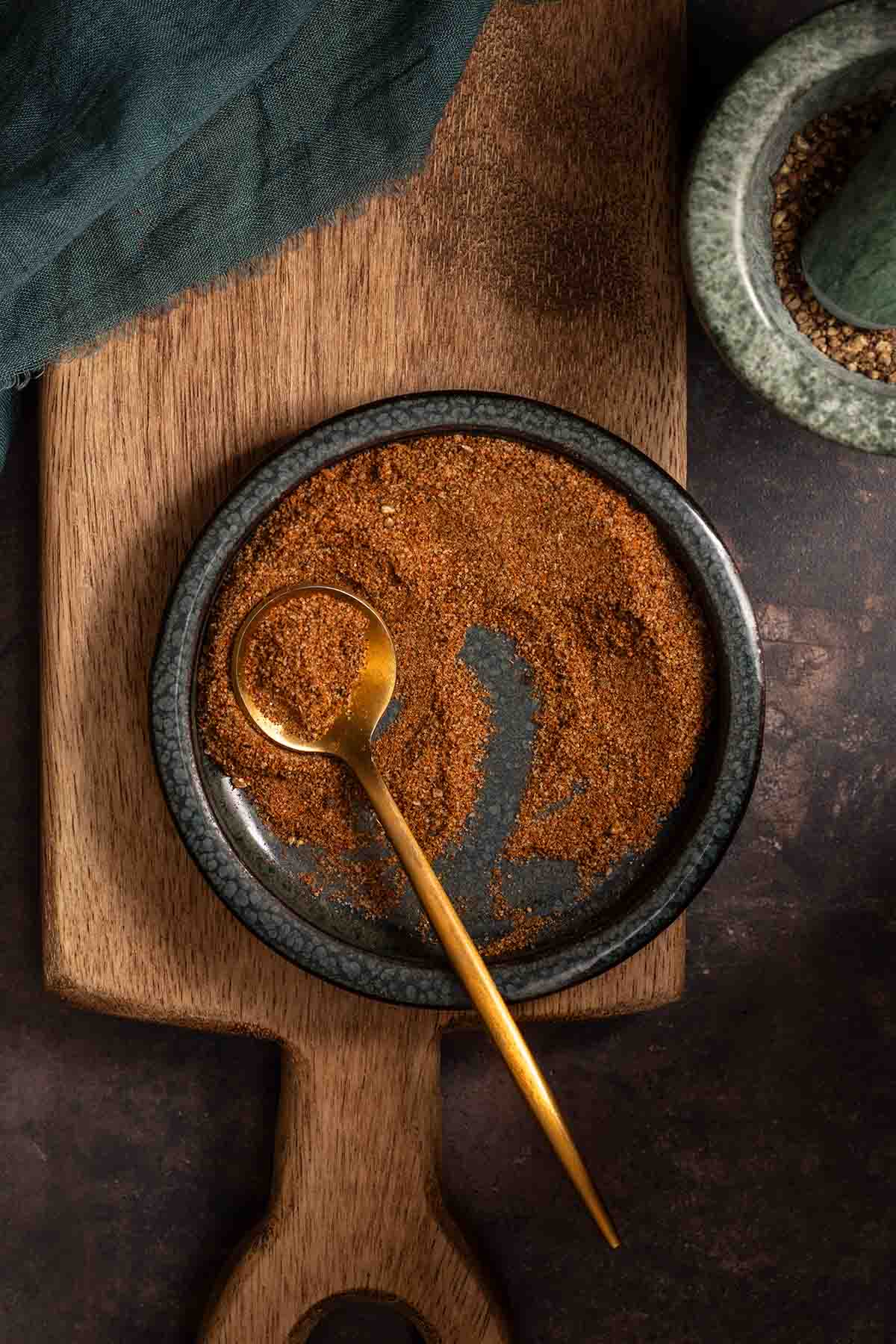 A small bowl of homemade Old Bay seasoning on a wooden cutting board.