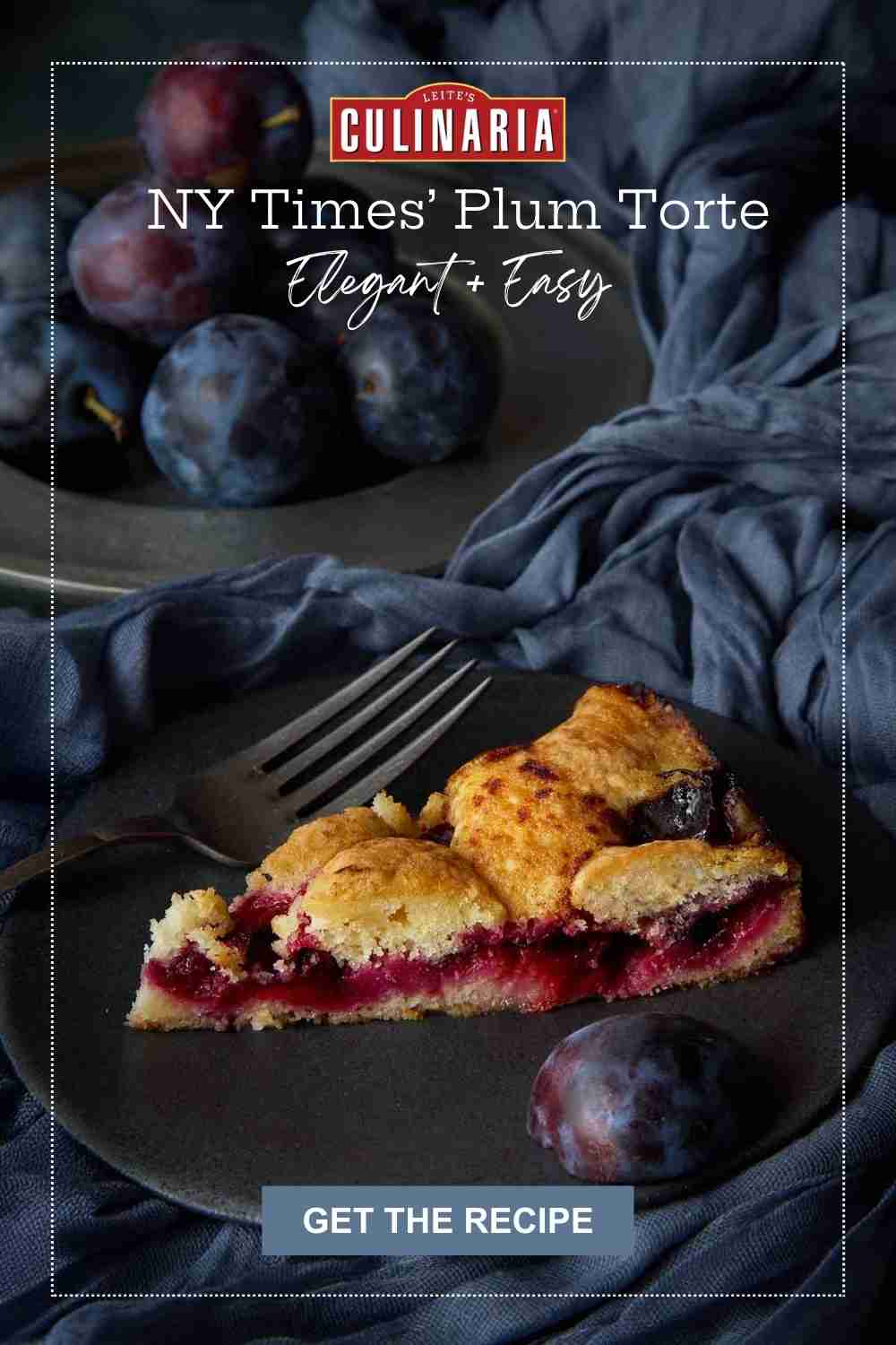 A slice of a plum tart on a gray plate with a pile of plums behind.