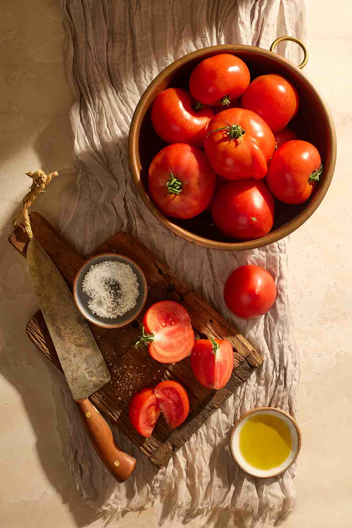 Ingredients for tomato paste, including fresh tomatoes, salt, and olive oil on a wooden board.