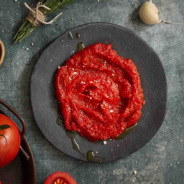 A dark plate with a mound of homemade tomato paste drizzled with olive oil and sprinkled with salt.