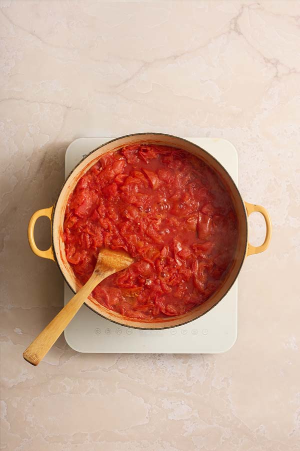 Chopped tomatoes boiling and softening in a large yellow pot to release their juices.