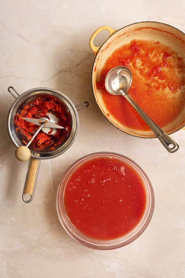 Passing cooked tomatoes through a food mill to create a smooth purée and remove skins and seeds.