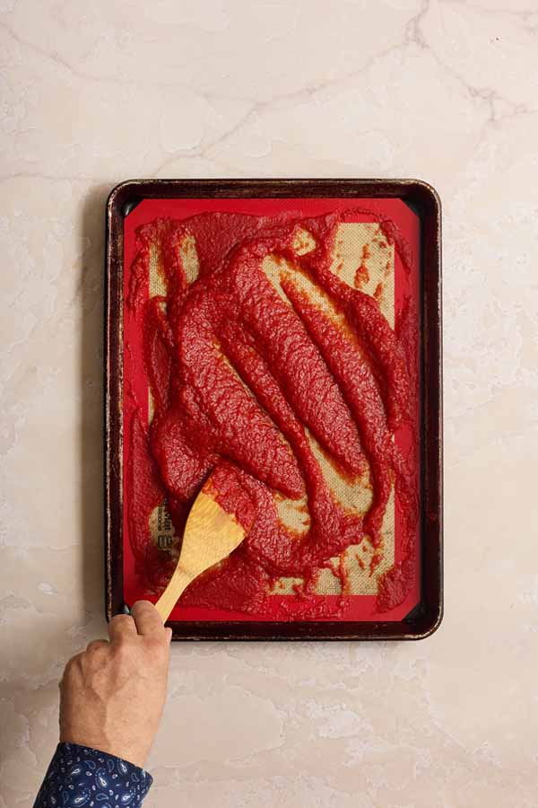 Stirring the tomato paste on the baking sheet partway through the baking process to ensure it dries evenly.