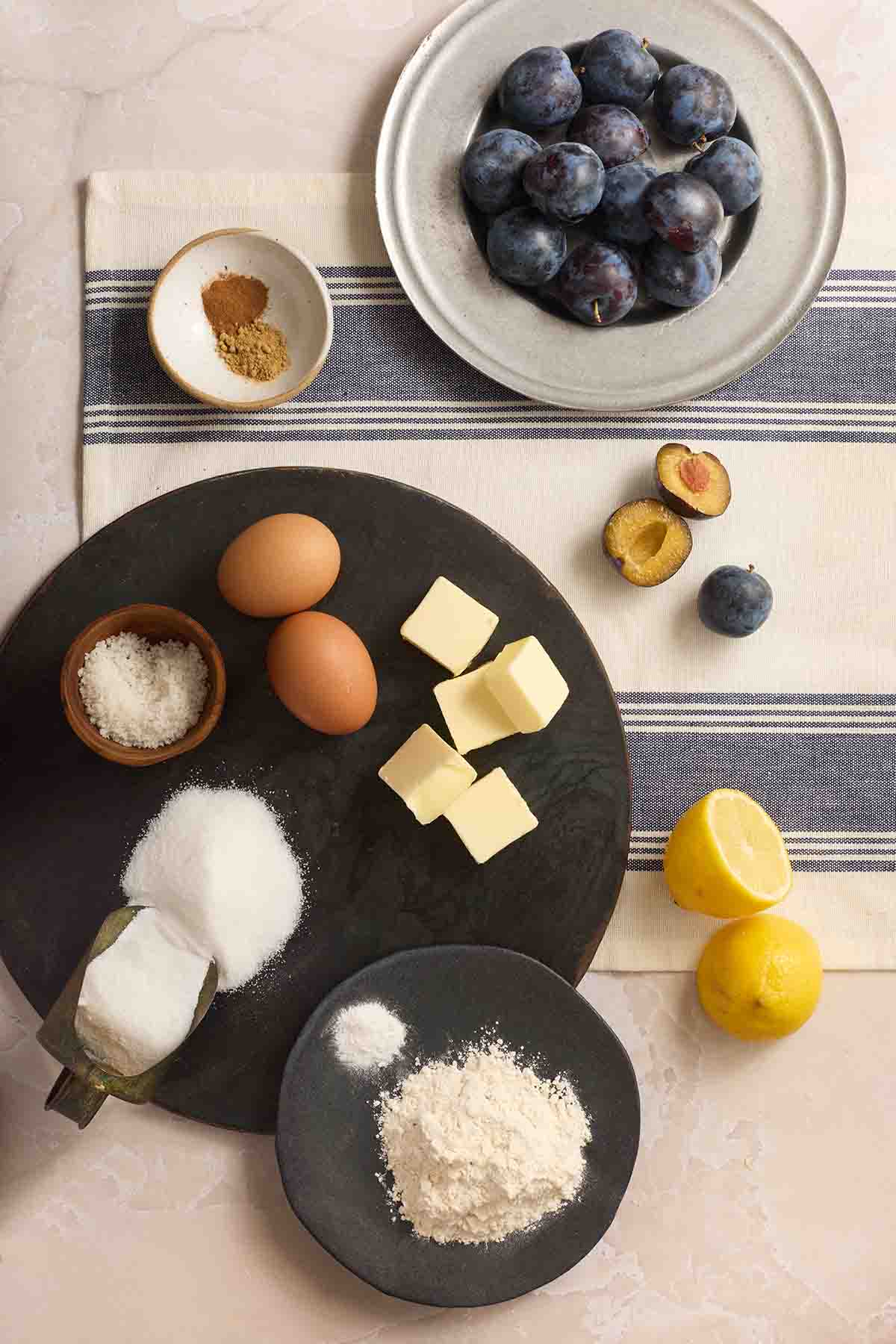 Ingredients for plum torte including flour, sugar, butter, eggs, lemons, and fresh plums.