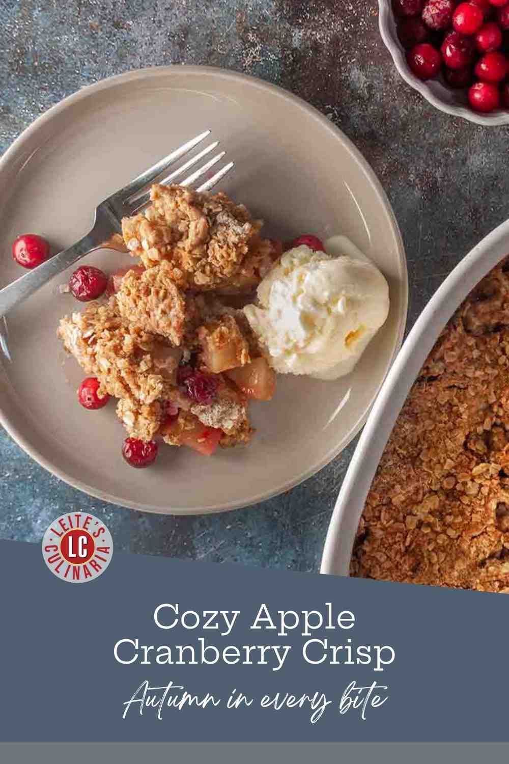 A portion of baked apple and cranberry crisp with an oatmeal-pecan topping served on a plate with a melting scoop of vanilla ice cream.