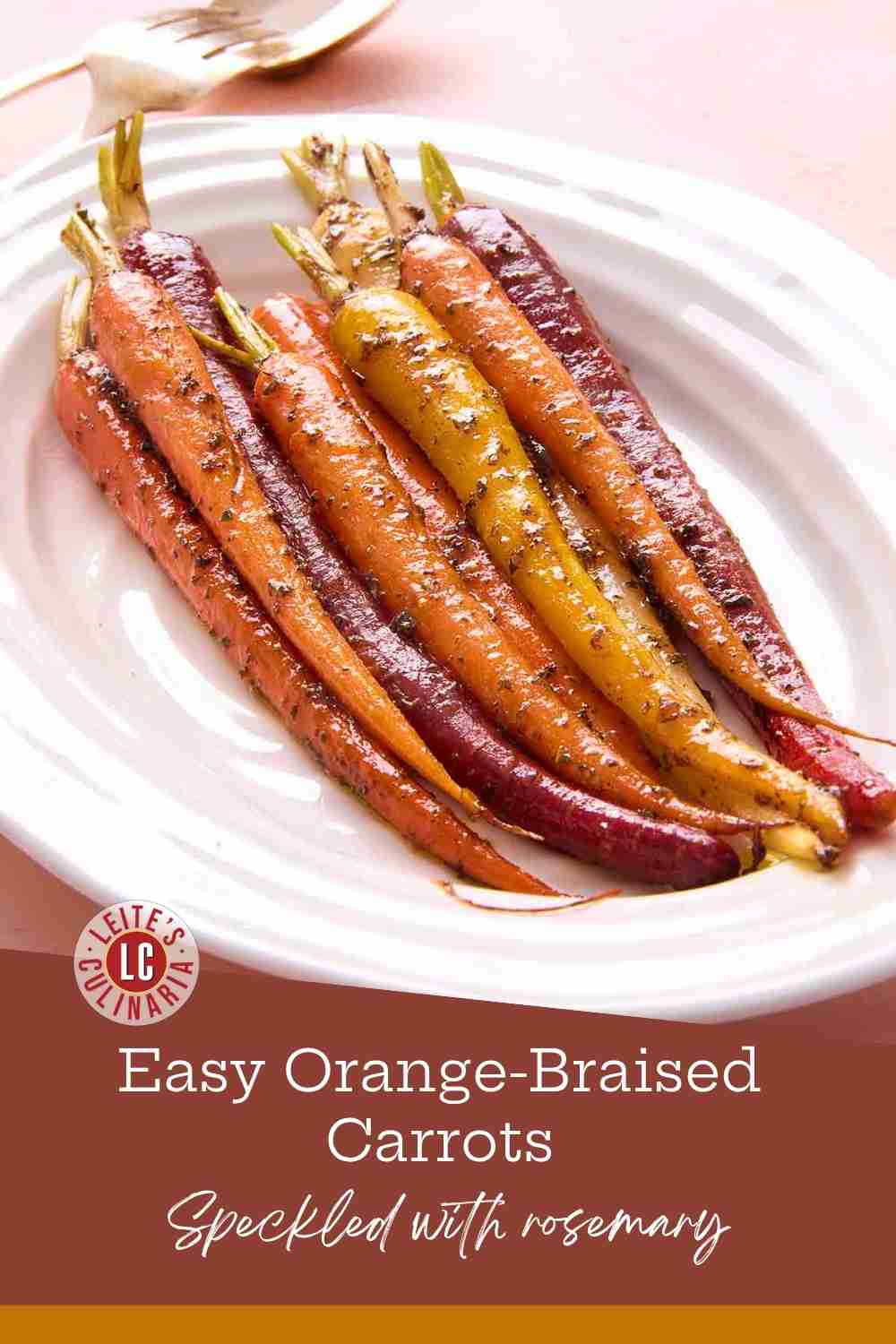 A beautiful side dish of slender, multi-colored braised carrots garnished with fresh rosemary on a white serving platter.