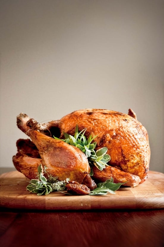 A whole deep-fried turkey, garnished with sage, bay, and thyme leaves on a wooden cutting board.