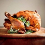 A whole deep-fried turkey, garnished with sage, bay, and thyme leaves on a wooden cutting board.