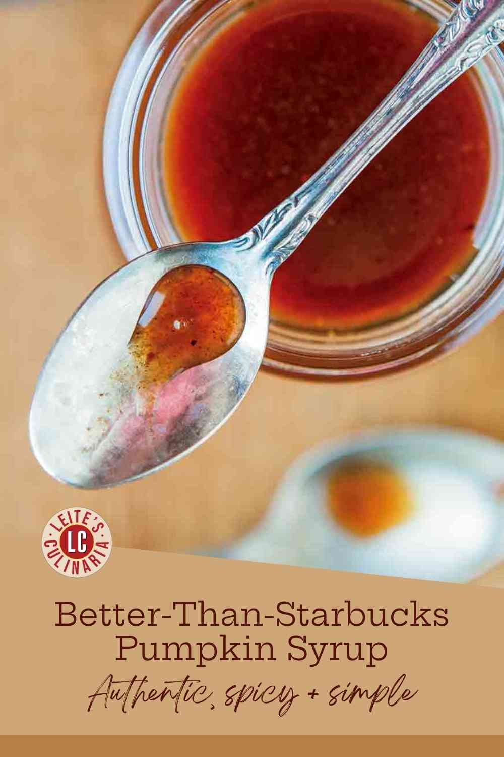 A spoon of homemade pumpkin spice syrup resting on a jar of syrup on a light wooden background.