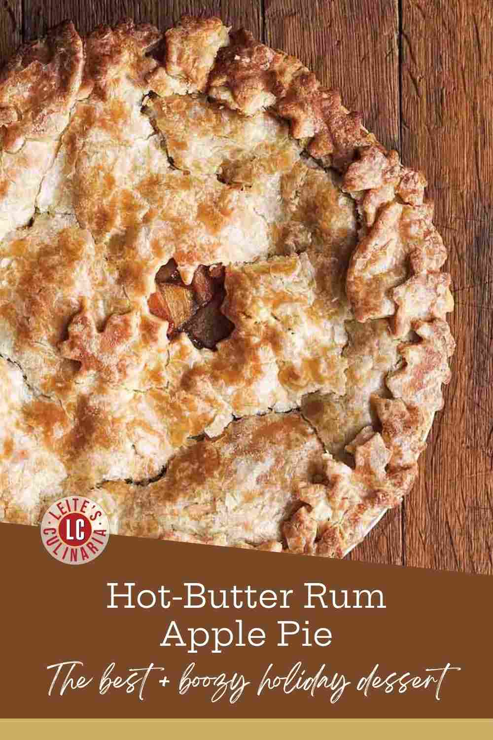 A baked apple pie with a flaky, golden-brown crust sits on a dark wooden board, cooling on a wire rack.