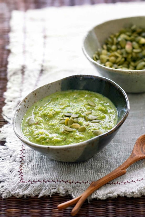 Pumpkin seed mole verde in a rustic ceramic bowl topped with pepitas, with a wooden spoon alongside.