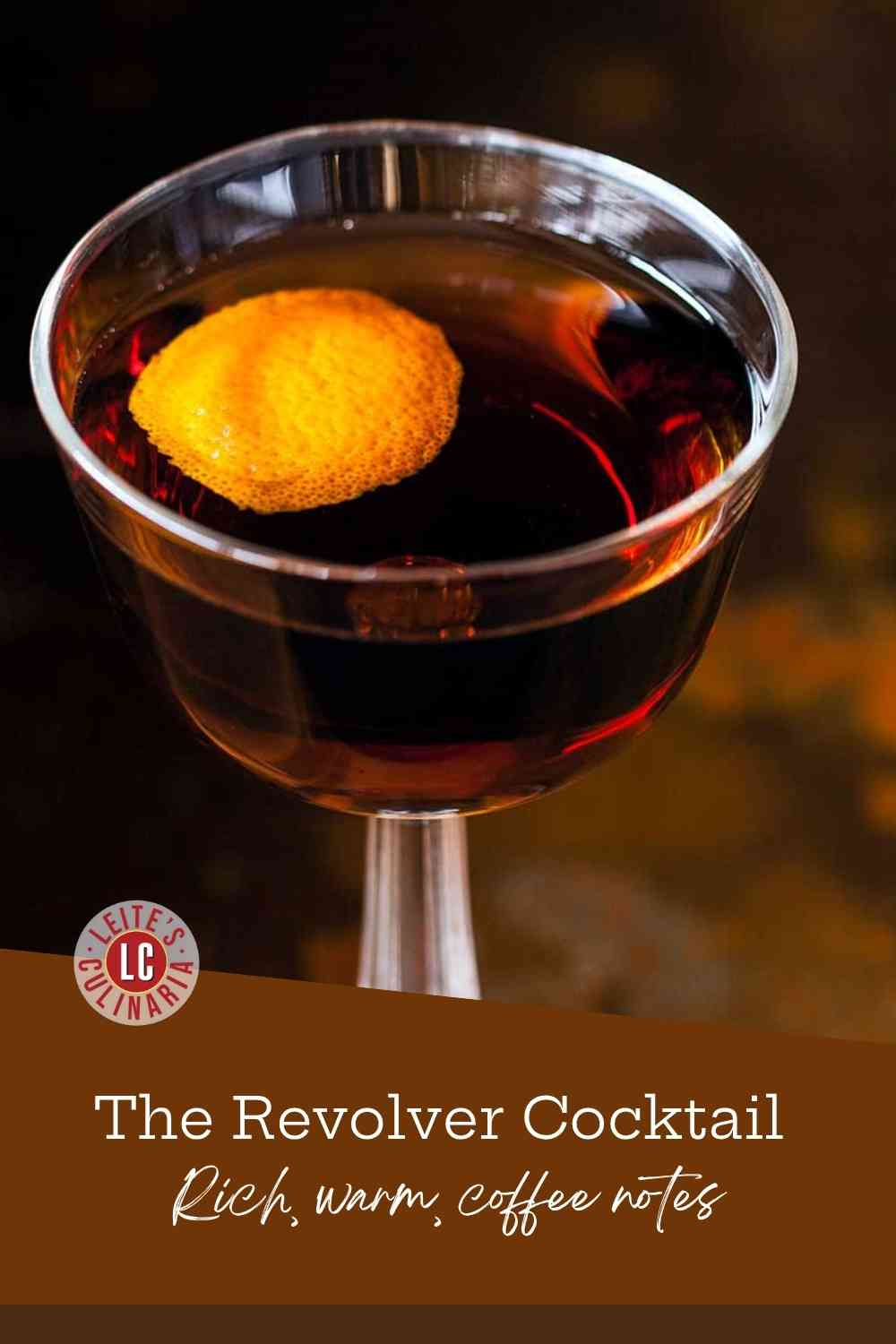 A coupe glass holds a dark, stirred bourbon and coffee liqueur cocktail, beautifully garnished with an aromatic flamed orange peel.