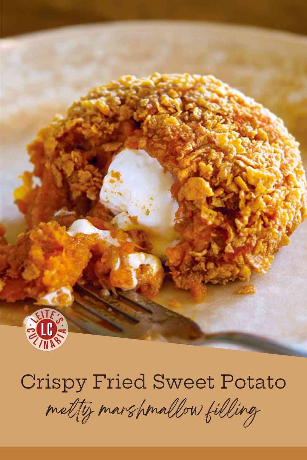 A fried, cornflake-crusted sweet potato ball broken open, showing the melted white marshmallow filling and warm, orange mash.