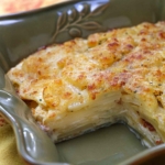 A dish of celeriac gratin, with a pieced removed, showing the layers, and creamy cheese filling.