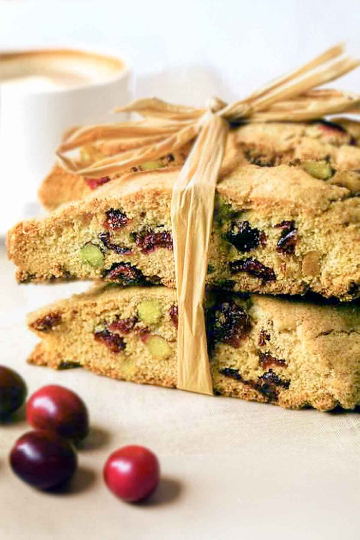 A stack of cranberry pistachio biscotti cookies tied together with raffia. with cranberries scattered around.