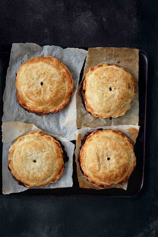 Four individual mushroom wellingtons with spinach and walnuts on a squares of parchment paper.