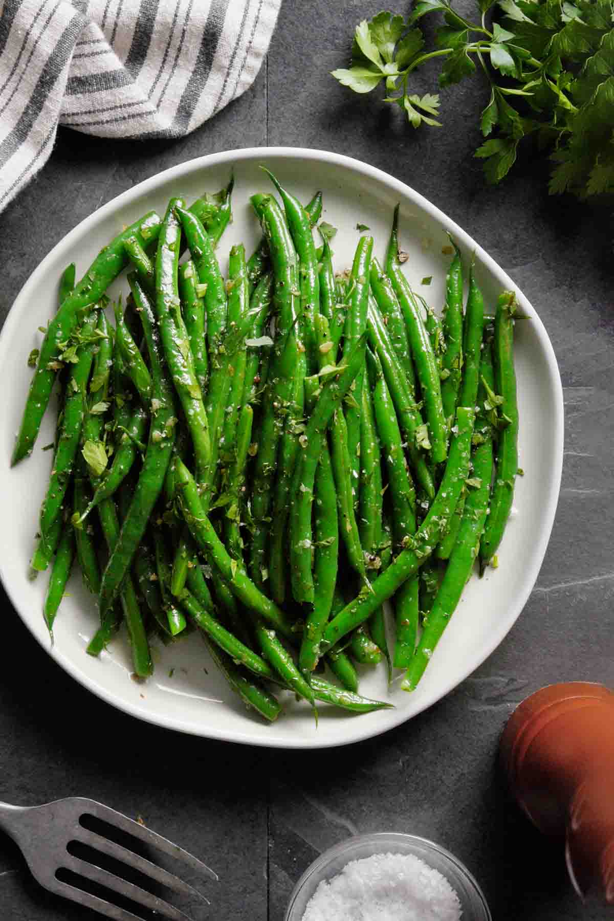 A white plate of buttered pan-fried green beans sprinkled with parsley and sea salt.