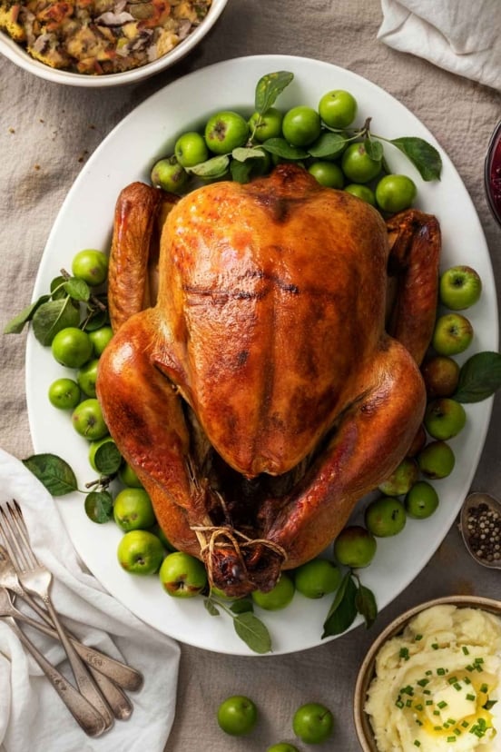 A golden-brown Thanksgiving turkey in the center of a table with napkins and bowls nearby.