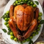 A Thanksgiving turkey on a white platter in the center of a table with side dishes nearby.