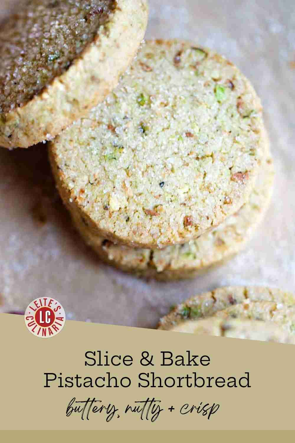 Stack of round, sugar-crusted pistachio shortbread cookies on parchment with cracked pistachios scattered nearby.