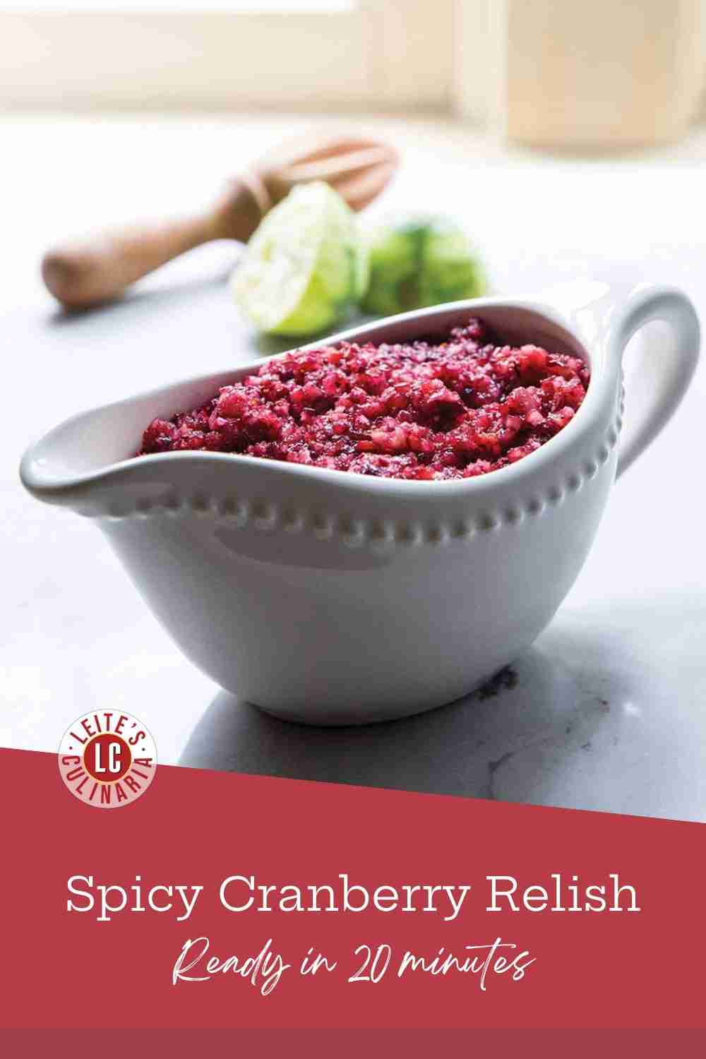 Raw cranberry relish in a white ceramic gravy boat, with a lime juicer and half-lime in the background.
