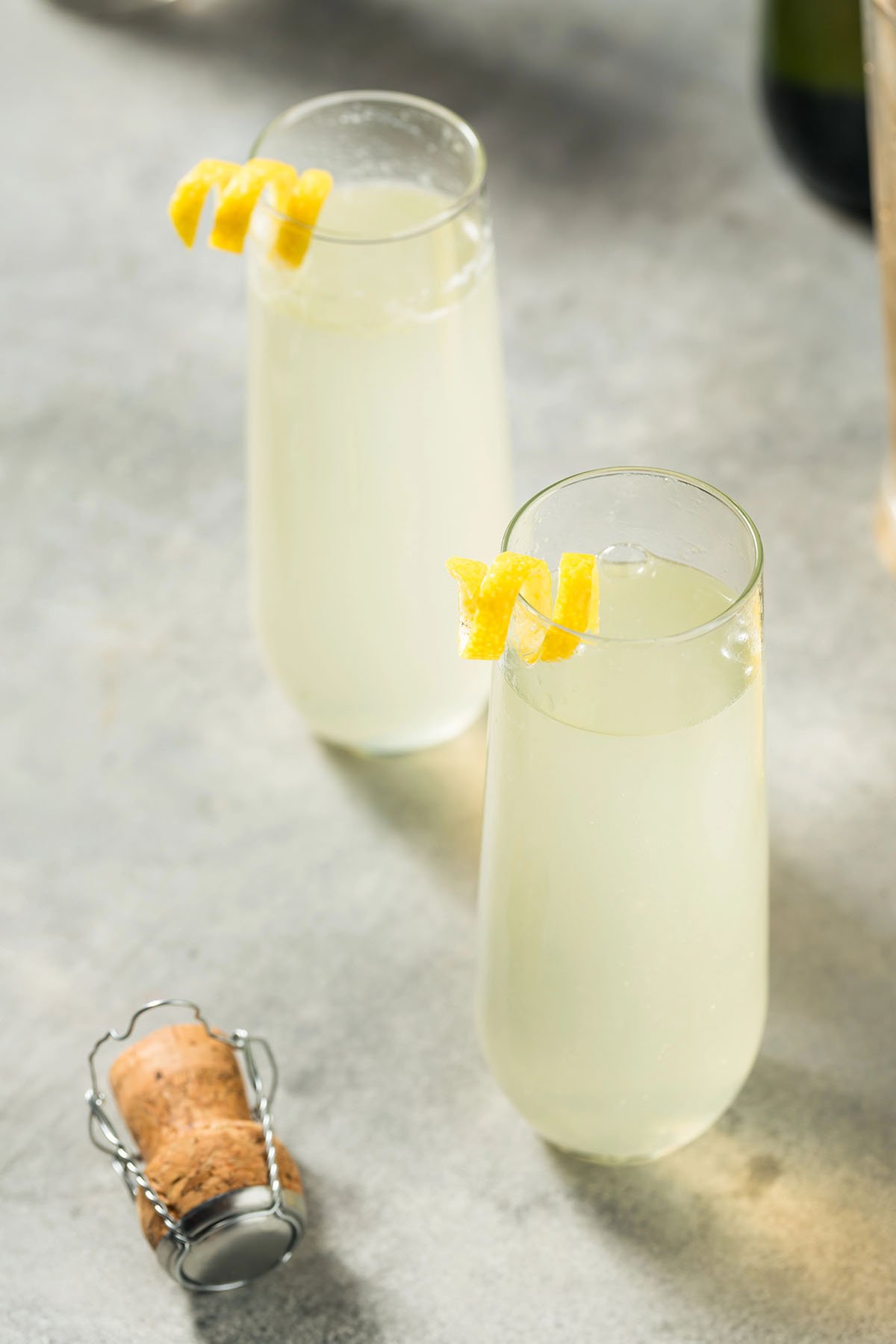 Two stemless flutes filled with a batched classic French 75 cocktail and lemon twists.