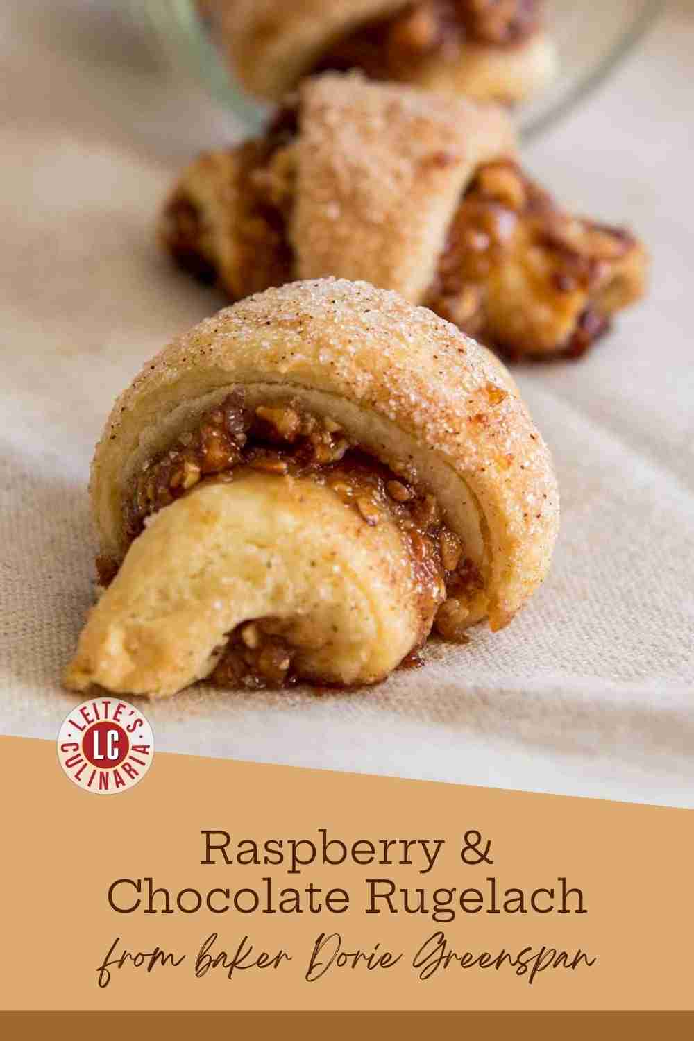 Flaky rugelach pastry sprinkled with decorating sugar, revealing the jam, chopped nut, and chocolate filling.