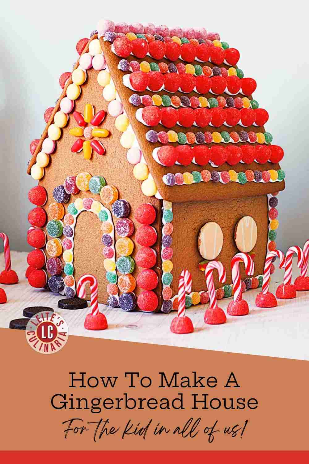 An elaborately decorated gingerbread house with a red candy roof, colorful gumdrops, and candy cane accents.
