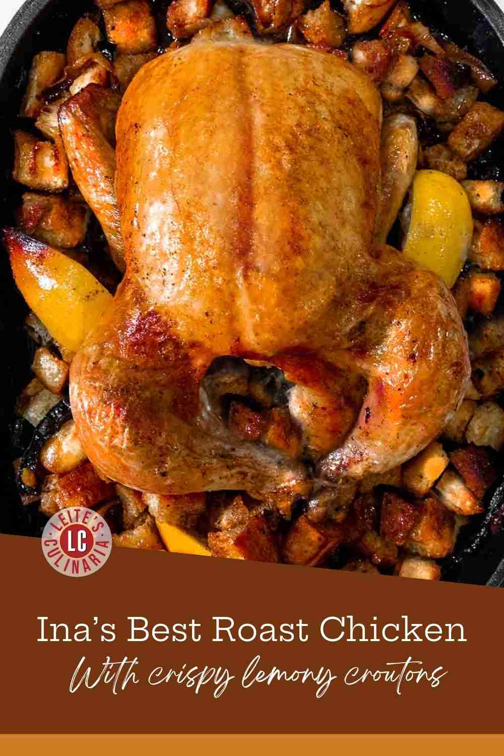 A whole roasted golden chicken in a cast iron pan surrounded by toasted bread croutons and lemon wedges.